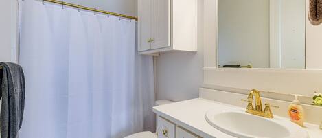 A bathroom with a white toilet, a white sink with a gold faucet, and a white shower curtain.