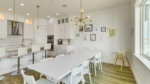 A modern kitchen with white cabinetry, a long dining table, and a chandelier. - Walk to Beaches: Padre Island Escape w/ Dock (Corpus Christi)