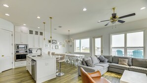 A modern kitchen with white cabinets, a central island, and a dining area with a white table and chairs. - Walk to Beaches: Padre Island Escape w/ Dock (Corpus Christi)