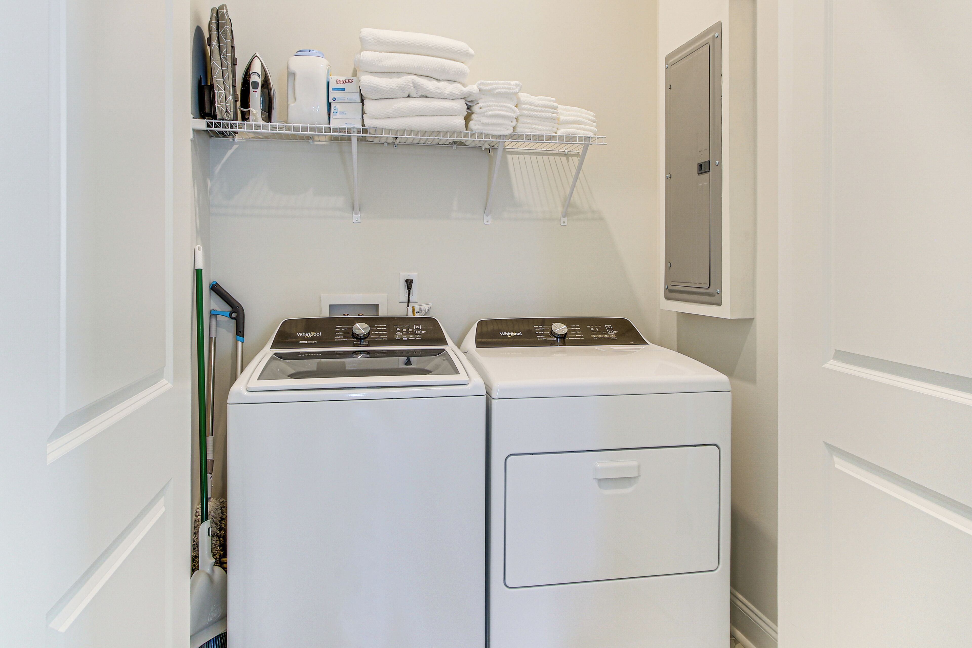 A laundry area with two front-loading washers and dryers, a shelf with folded towels, and a utility cabinet.