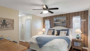 Une chambre à coucher comprenant un lit, des tables de chevet, un ventilateur de plafond et un panneau mural en bois.