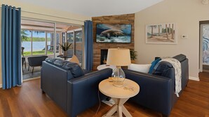 Un salon moderne avec un canapé bleu, une table ronde en bois et une grande fenêtre donnant sur une étendue d’eau.