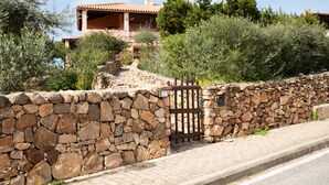 A stone wall with a gate, a paved path, and a building with a tiled roof in the background.