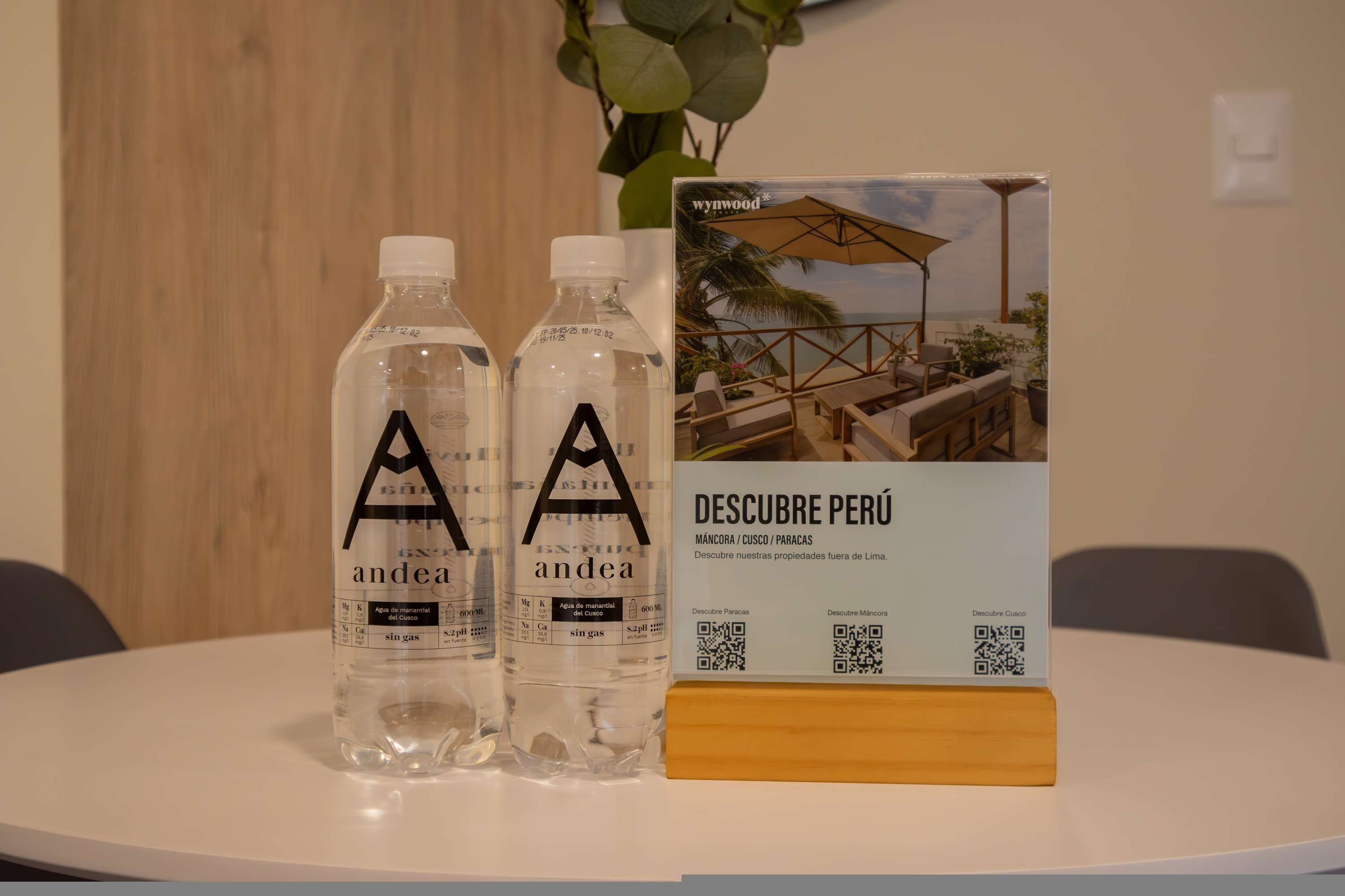 Zwei mit 'andea' beschriftete Flaschen auf einem Tisch, zusammen mit einer Broschüre mit dem Titel 'DESCUBRE PERÚ' und einem QR-Code.