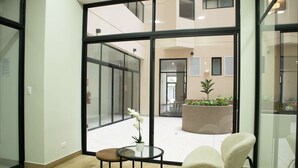 Un interior moderno con amplios ventanales que dan a un espacio exterior, una pequeña mesa redonda con un jarrón y una silla acolchada.