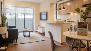 Una sala de estar moderna con sofá, una mesa de centro y un comedor con sillas y una mesa. Hay un ventanal grande que proporciona luz natural y vistas al exterior.