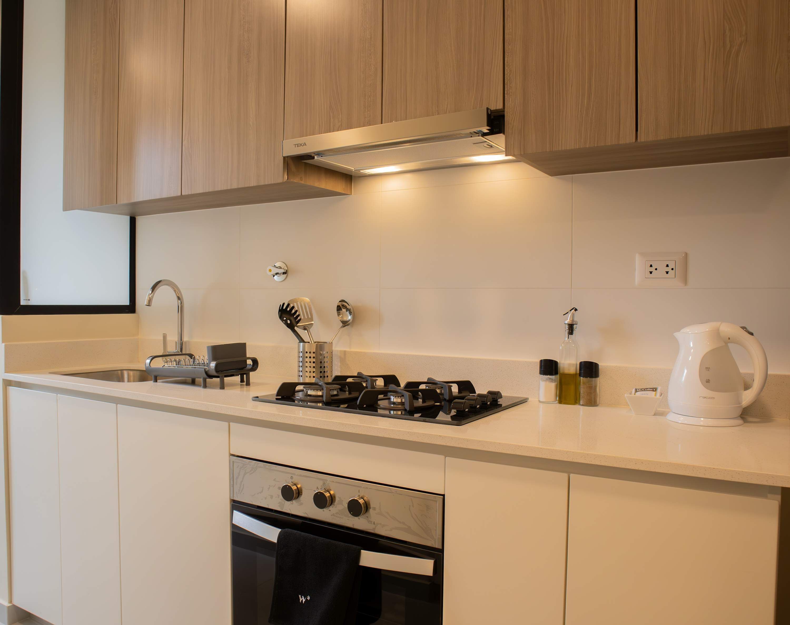 A modern kitchen with wooden cabinets, a stainless steel sink, a gas stove, and a kettle.