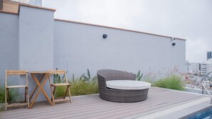 Una terraza en la azotea con piscina, un sofá de mimbre y una mesa de madera.