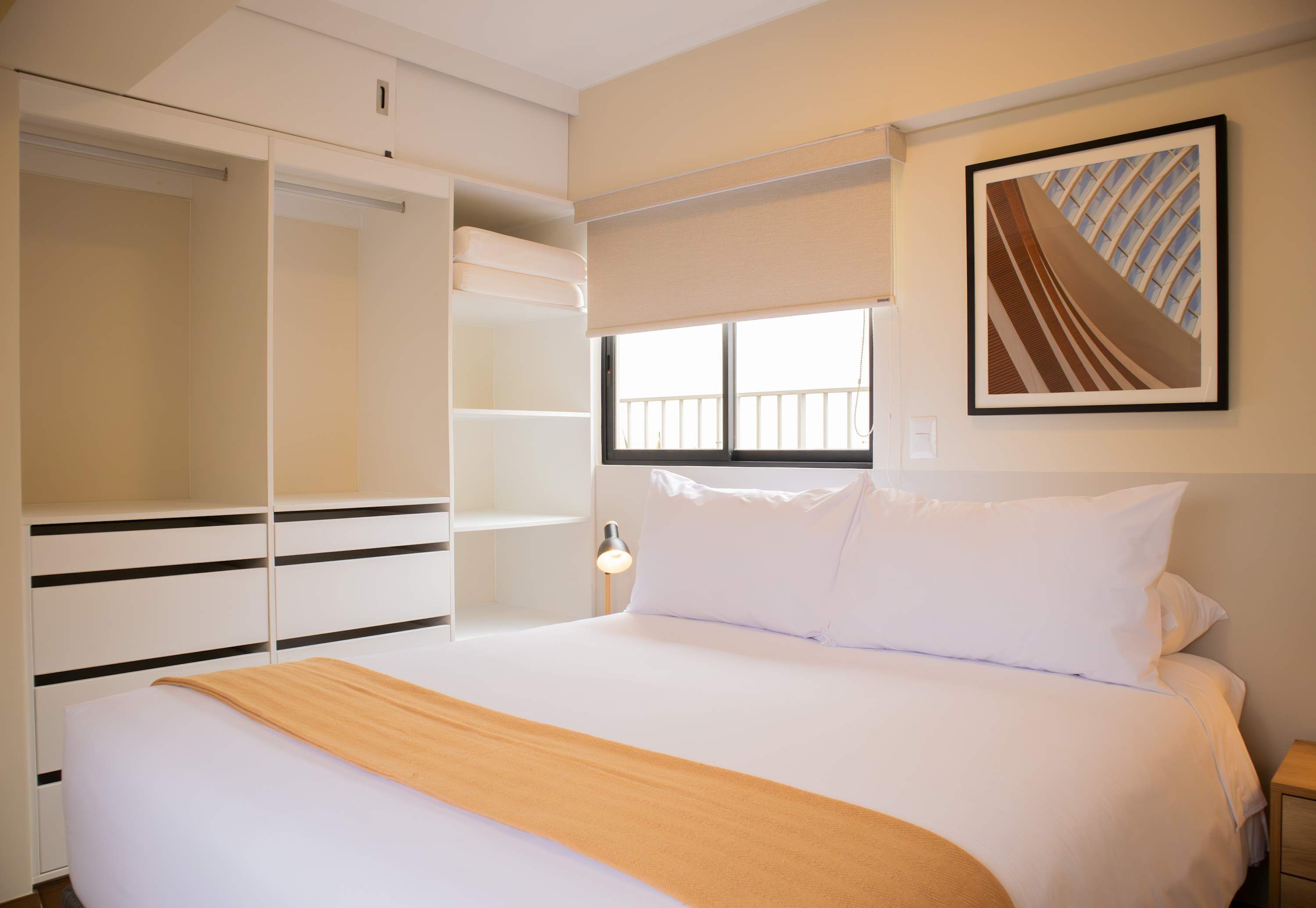 Habitación de hotel con una cama grande, un armario con varios compartimentos, una ventana con vistas y un cuadro en la pared.