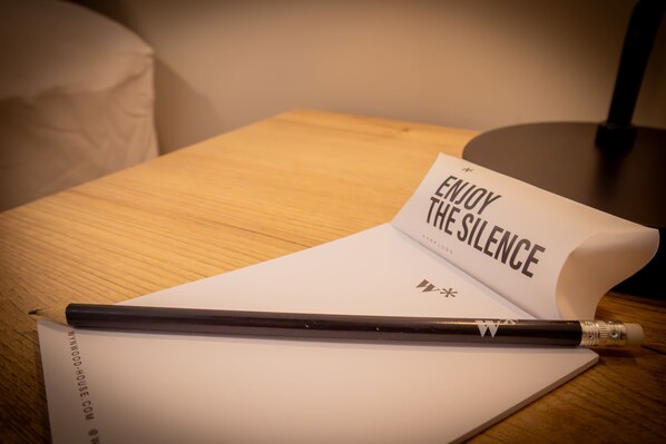 Una mesa de madera con una hoja de papel blanco, un bolígrafo negro y un libro titulado 'ENJOY THE SILENCE'.