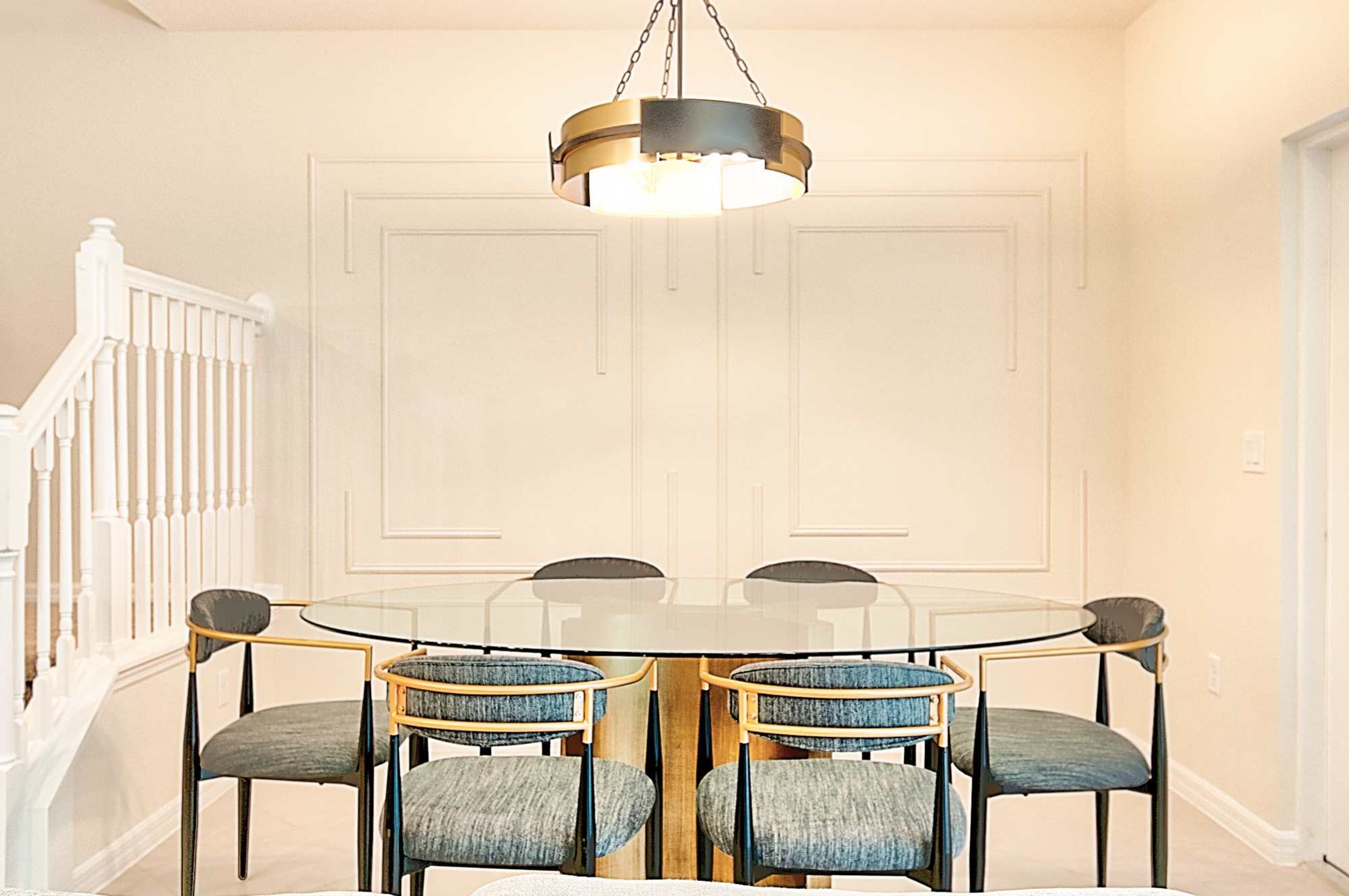 A dining area with a round glass table, six chairs, and a central hanging light fixture.