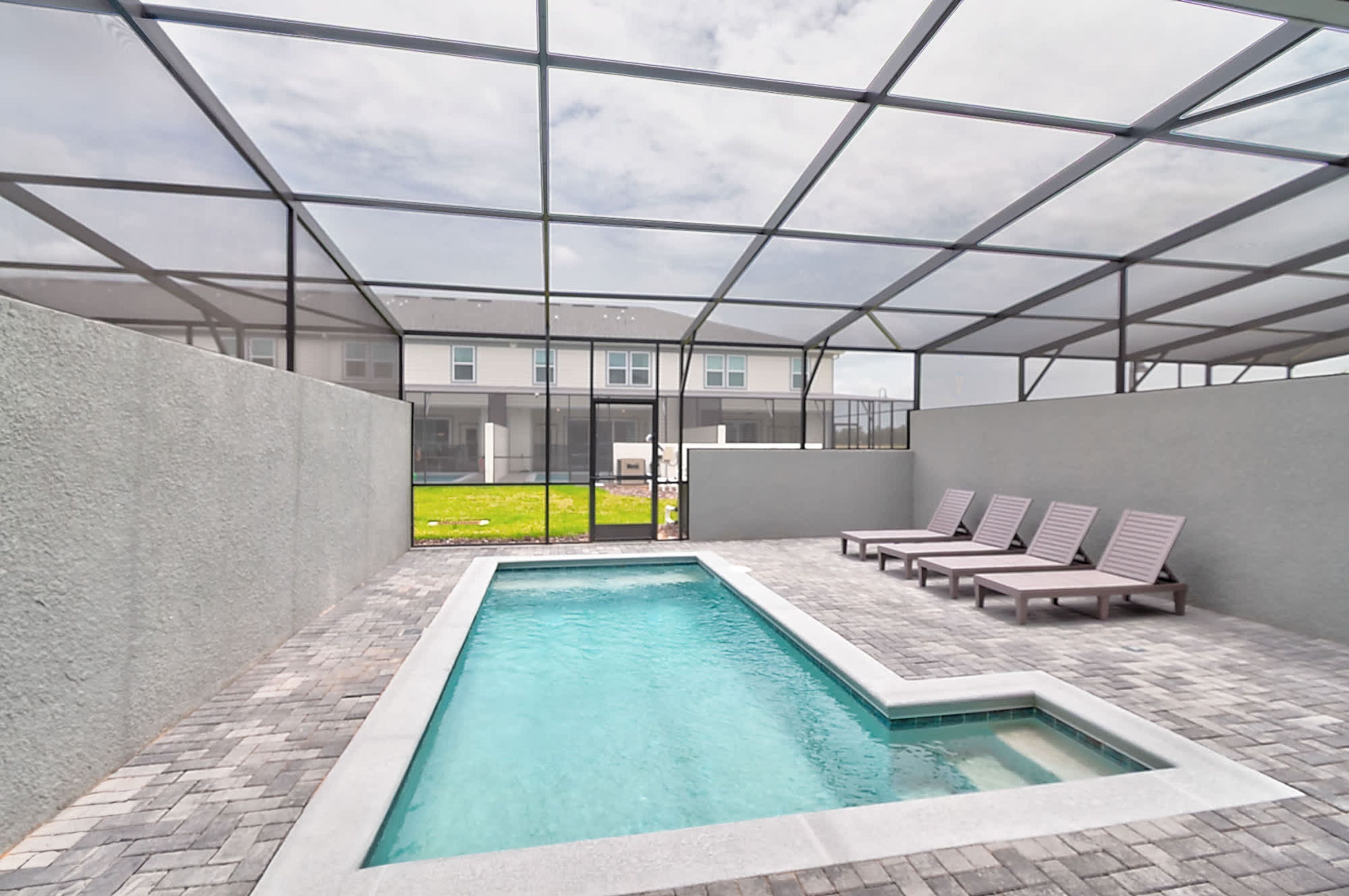 A pool area with a glass enclosure, lounge chairs, and a view of a building in the background.
