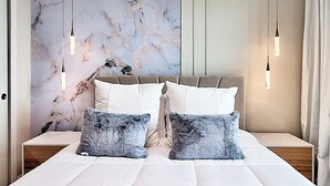 A bedroom with a marble wall, a tufted headboard, two bedside tables, and hanging light fixtures. - 16037 Dream Vacation Family Home 5BD (Clermont)