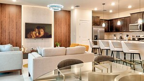 A modern living room with a sofa, a glass coffee table, and a dining area with chairs and a kitchen in the background. - 16037 Dream Vacation Family Home 5BD (Clermont)