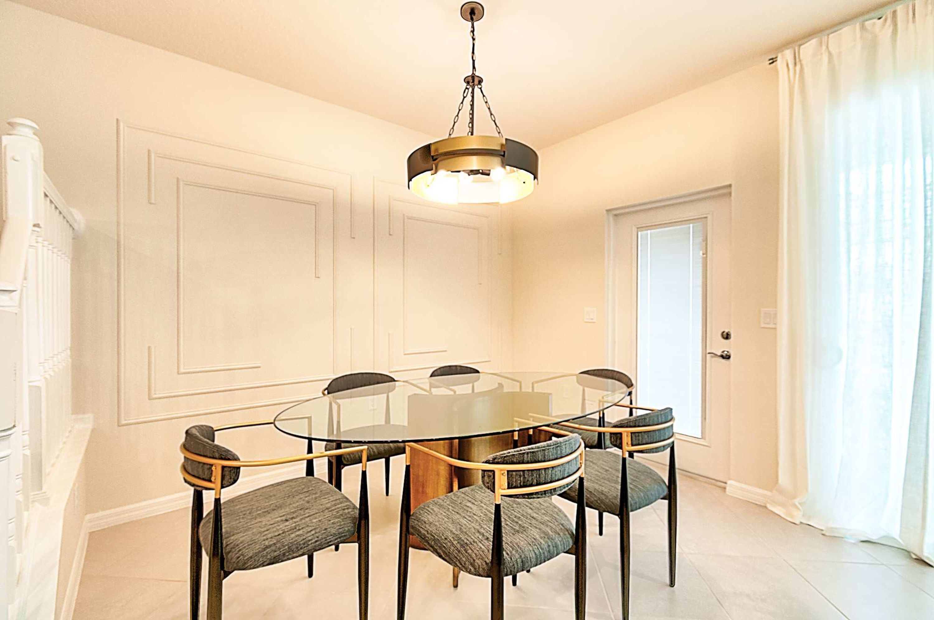 Une salle à manger avec une table ronde en verre entourée de six chaises, un lustre et une porte blanche.