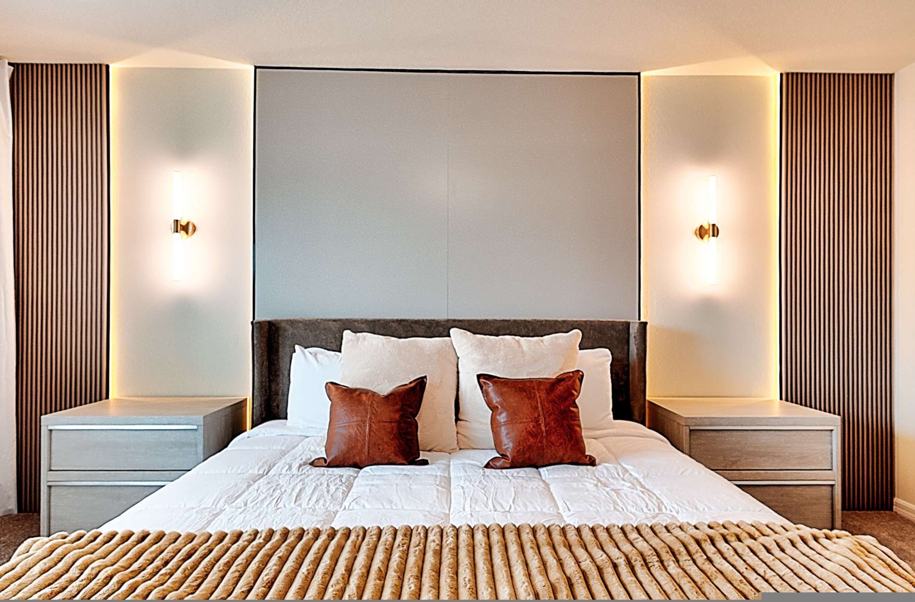 A modern hotel room with a large bed, two nightstands, and wall-mounted lighting.