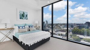Ein modernes Schlafzimmer mit einem großen Bett, Blick auf die Stadt und einem Deckenventilator.