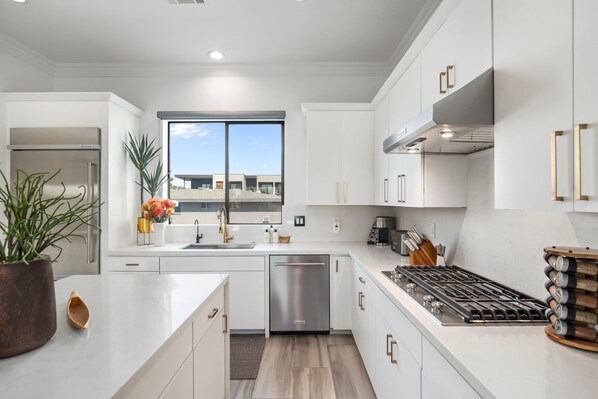 A modern kitchen with white cabinetry, stainless steel appliances, and a large window providing a view of the outside.