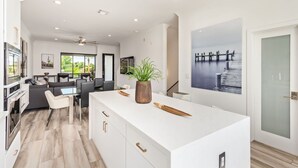 A modern kitchen with a white island, dining area, and a large window. - NEW Desert Standard Modern 3-level Oasis (Scottsdale)