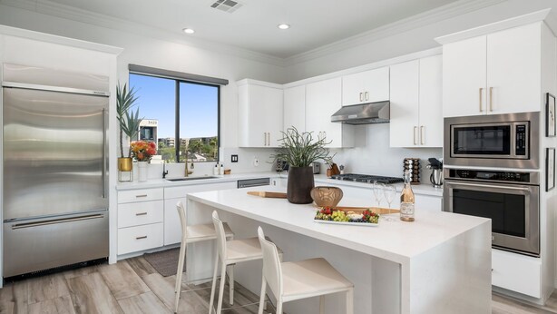 A modern kitchen with white cabinetry, stainless steel appliances, a large island with seating, and a view of the city. - NEW Desert Standard Modern 3-level Oasis (Scottsdale)