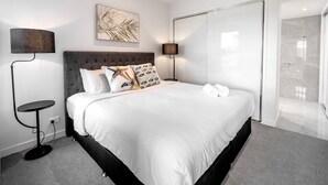 A modern hotel room with a large bed, two bedside lamps, a wall art piece, and a sliding door leading to a balcony. - 3BR Lux Beachfront Escape - Pool Gym King bed (Sunshine Coast)