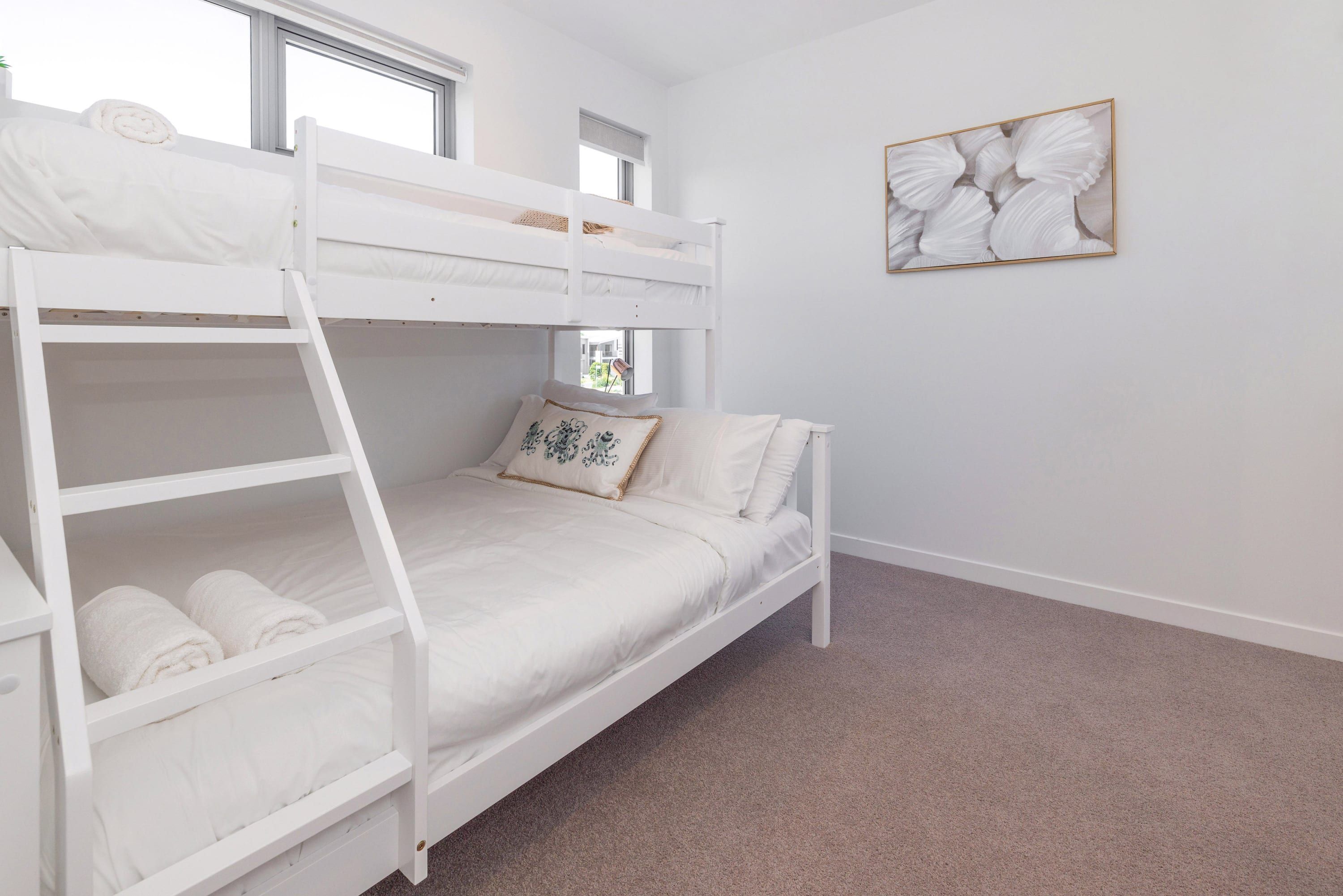 A bunk bed room with a ladder, a window, and a framed artwork on the wall.