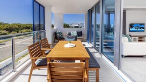 A balcony with a wooden table and chairs, a sofa, and a television. - 3BR Lux Beachfront Escape - Pool Gym King bed (Sunshine Coast)