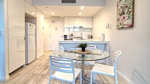 A modern kitchen with white cabinets, a glass dining table, and white chairs. - 2BR Food Drink Hub Pool Parking Gym Rooftop (Brisbane)