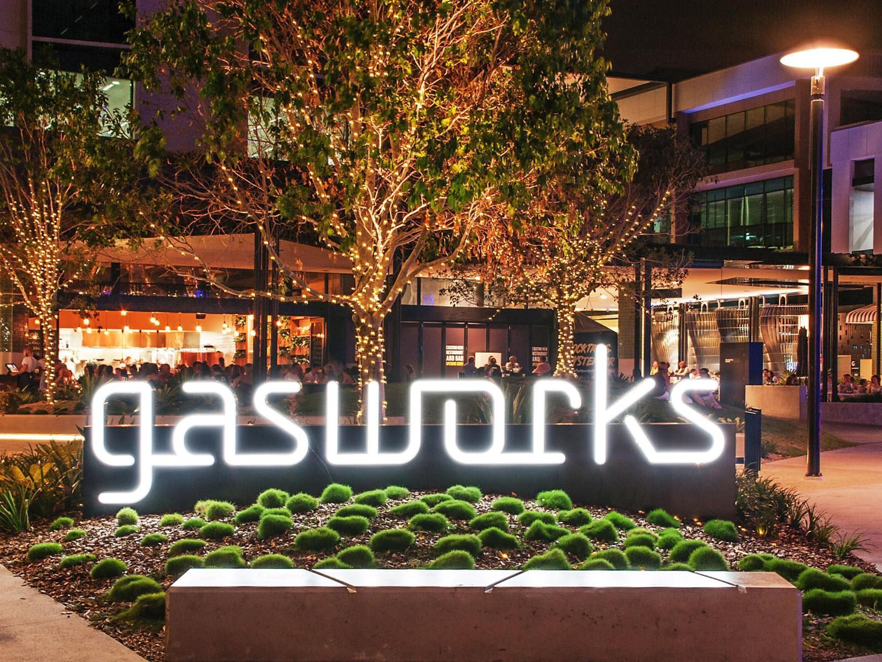 A nighttime view of a commercial area with illuminated signage for 'gasworks' and surrounding buildings.