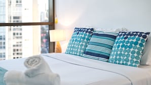 A neatly made bed with blue and white pillows, a rolled white towel, and a lamp on a bedside table. - 2BR Food Drink Hub Pool Parking Gym Rooftop (Brisbane)