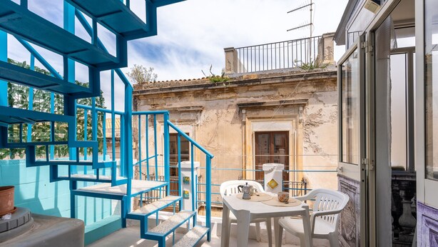A balcony with a blue staircase, a table with chairs, and a view of a historic building.