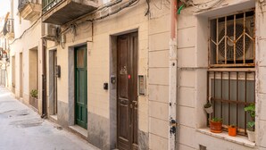 A narrow street with buildings featuring traditional architecture, including balconies and potted plants.
