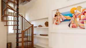 Una escalera de caracol con barandillas de madera y un pasamanos negro, que conduce a una pared blanca con estantes que exhiben objetos decorativos y un cuadro abstracto colorido.