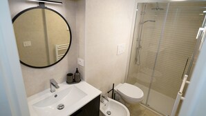 Une salle de bain moderne avec un grand miroir rond, un lavabo, un bidet et une douche à parois de verre.