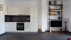 A modern kitchen with white cabinets, a black countertop, and a built-in oven. There is a wooden floor and a bookshelf with various items. - Tina's Penthouse by Wonderful Italy (Bari)