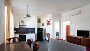 A modern kitchen with white cabinets, a black refrigerator, and a dining area with a wooden table and chairs. - Gil's Penthouse by Wonderful Italy (Bari)