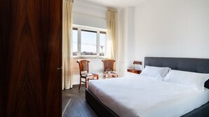 A hotel room with a large bed, two wooden chairs, a nightstand, and a window with curtains. - Gil's Penthouse by Wonderful Italy (Bari)