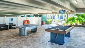 An indoor pool table area with two pool tables, seating, and a television screen.