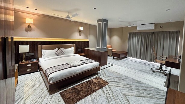 Hotelkamer met een groot bed, nachtkastjes, een bureau, een stoel, een staande lamp, een plafondventilator en een airconditioner.