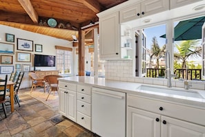A kitchen with white cabinetry, a large window, and a dining area with wicker furniture. - 30 secs to Beach, Ocean-view patio, Roof Deck (San Diego)
