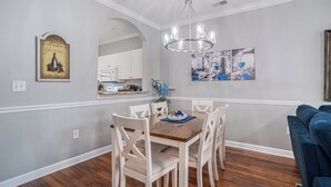 A dining area with a wooden table and white chairs, a chandelier, and artwork on the walls.