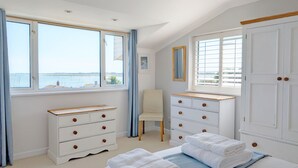 Une chambre avec une grande fenêtre, un lit, une commode et une chaise.