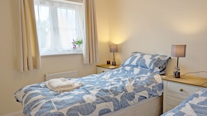A bedroom with a bed, bedside table, lamp, and window with curtains.