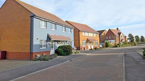 A residential street with houses featuring brick and siding exteriors, a paved road, and a clear sky.