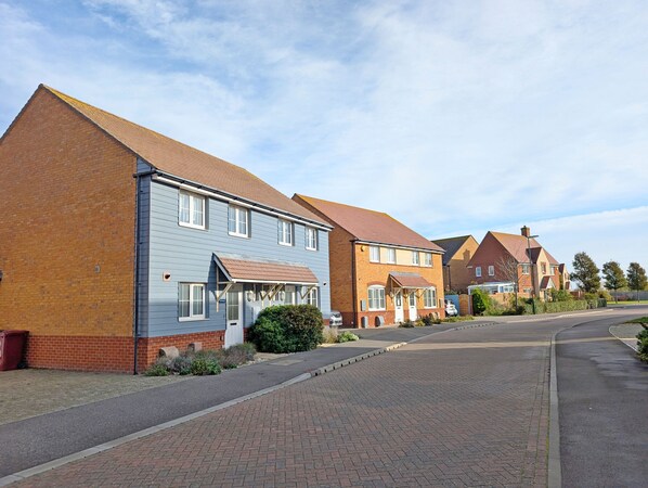 A residential street with houses featuring brick and siding exteriors, a paved road, and a clear sky.
