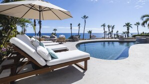 Ein Poolbereich mit Liegestühlen und Sonnenschirm, mit Blick auf einen klaren, blauen Himmel und das Meer.
