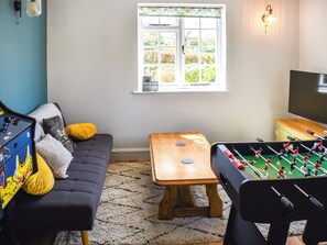 A room with a sofa, a foosball table, a television, and a window with a view of greenery.