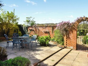 A patio with a brick wall, a metal gate, and a table with chairs. - 4 bedroom accommodation in Hanworth (Hanworth)