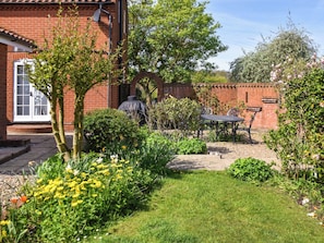 A garden with a brick wall, a covered outdoor seating area, and a variety of plants and flowers. - 4 bedroom accommodation in Hanworth (Hanworth)