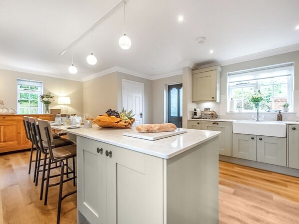 A modern kitchen with a central island, wooden chairs, a dining area, and a view of the outdoors.